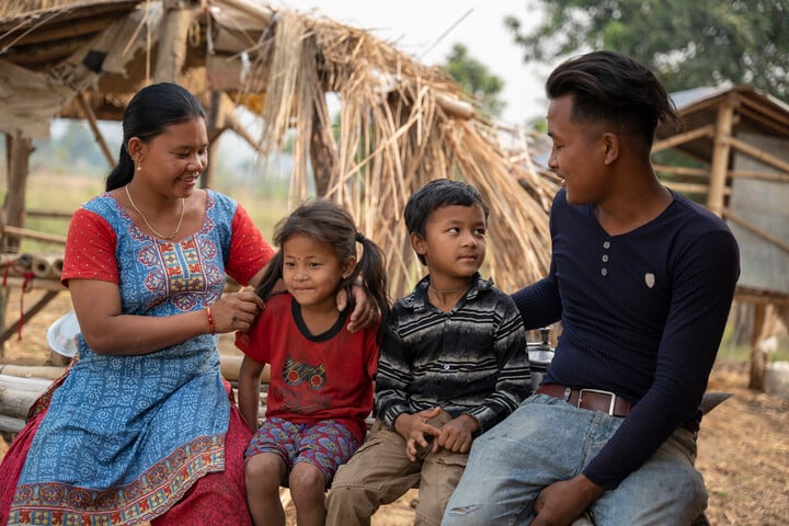 Sunil sitting outside his home with his mum, dad, and little sister – all together as a family.