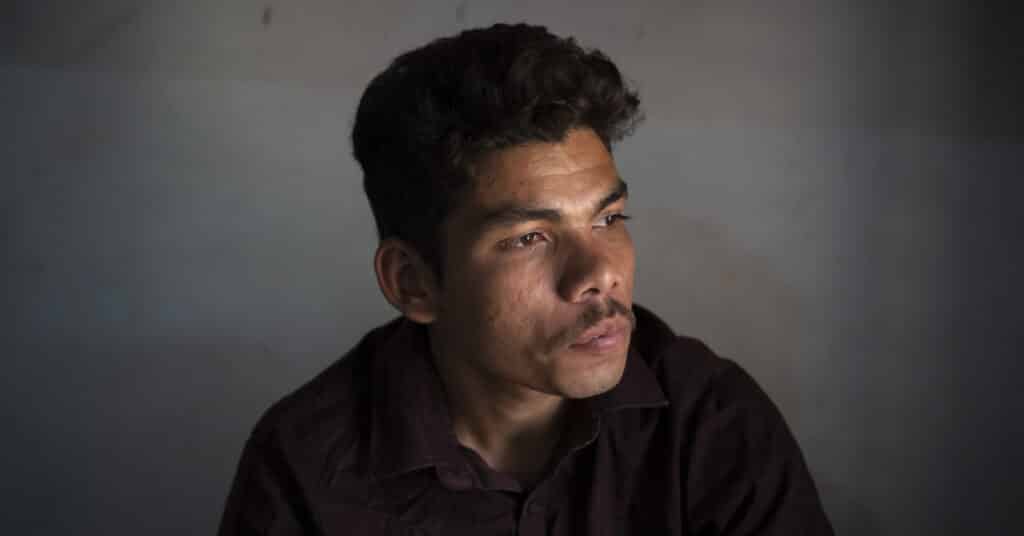 Young Nepali orphanage survivor Moti* sits against a grey wall in a darkened room. He's looking pensively to one side. He has short dark hair and a moustache and wears a dark brown shirt.