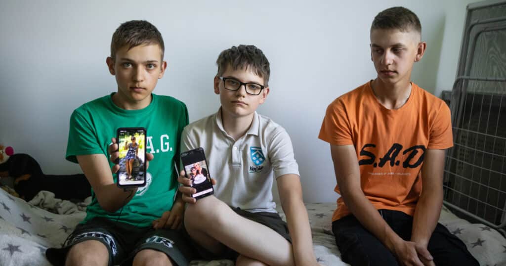 Mykhailo, Igor and Oleksi, three brothers, look sad as they hold up their phones displaying a photo of their deceased mum.