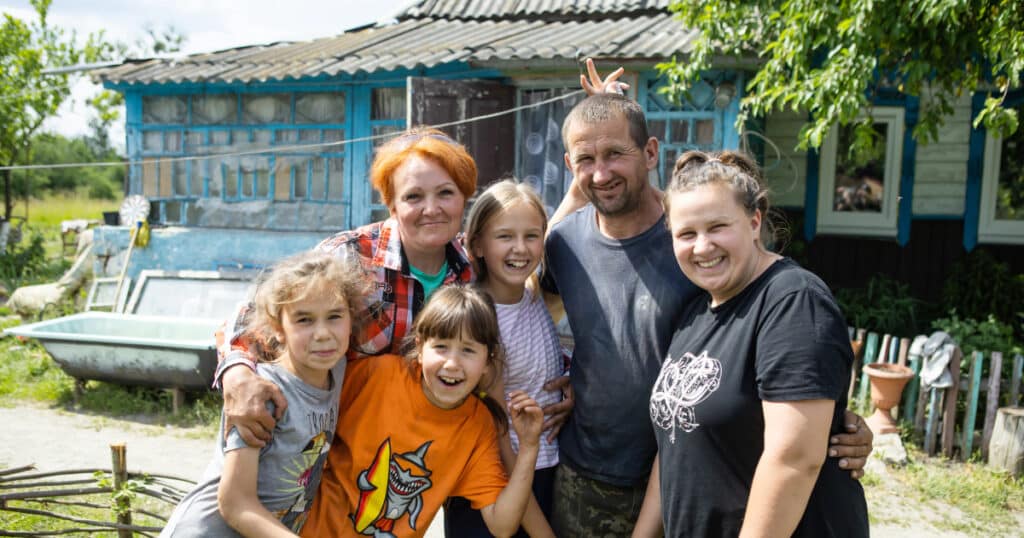 Lilia, Tina and their family smiling for a family photo outside their home, Ukraine.