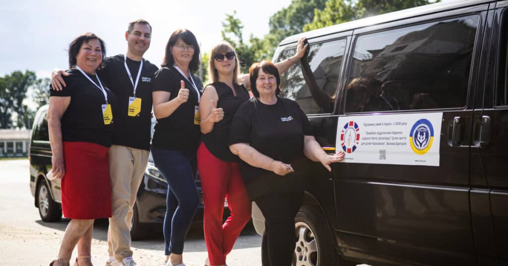 The Mobile Mental Health Team takes a group photo outside their black van, smiling on a sunny day.