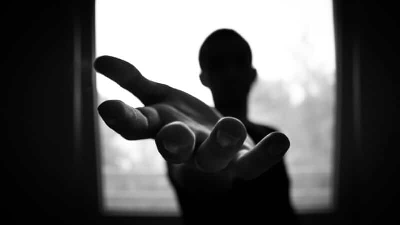 A young person in silhouette reaches out their hand towards the camera
