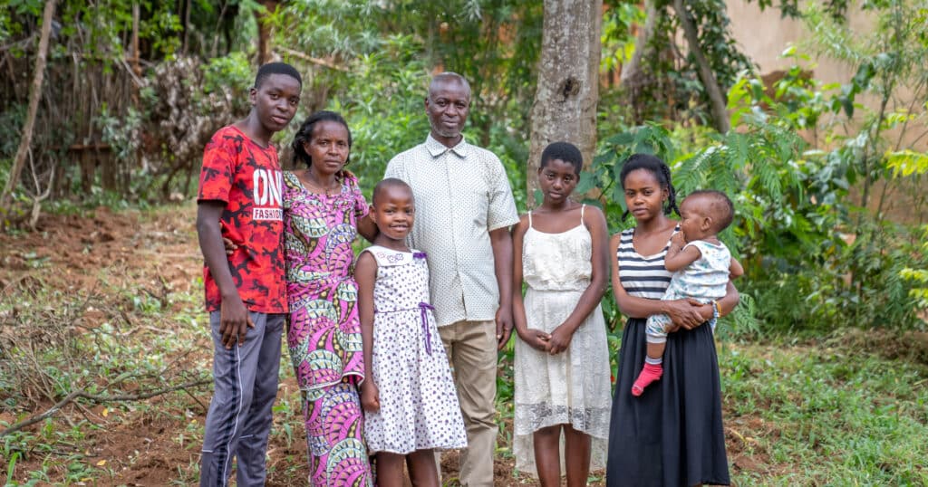 Uwase stands outside in her background with her foster family – her foster parents, brother, and two sisters. One of her sisters is holding a small baby – Uwase's niece.