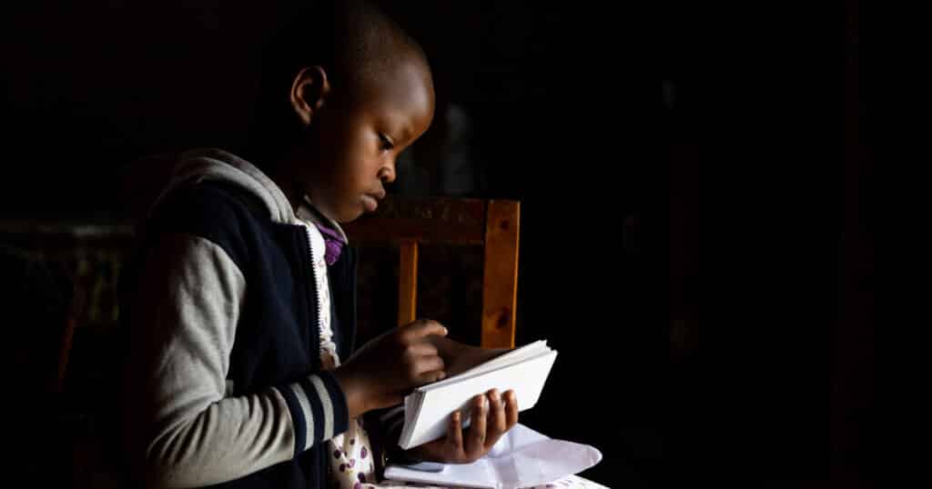 Uwase looks sad in a poorly lit room, turning away from the camera while filing through some pieces of paper.