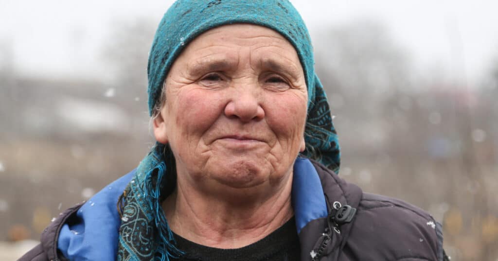 Gabriela, a woman in her late sixties, stares at the camera with a proud smile. She's wearing a turquoise headscarf. Snowflakes fall on her shoulder.