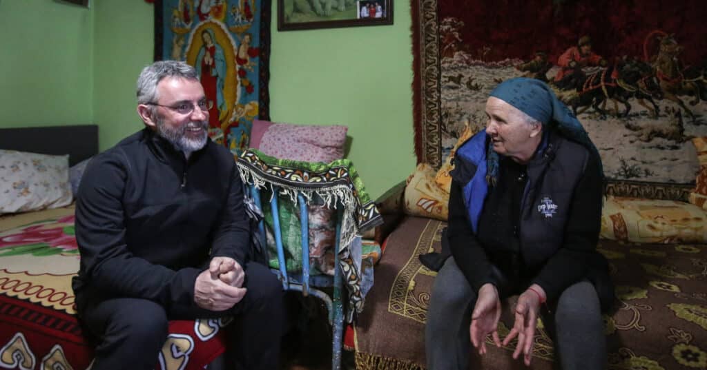 Radu Tohatan, HHC Social Worker, chatting with Gabriela in her home. The room is decorated with colourful tapestries and carpets.